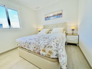 Een slaapkamer met een bed, twee nachtkastjes, een raam en een schilderij aan de muur.