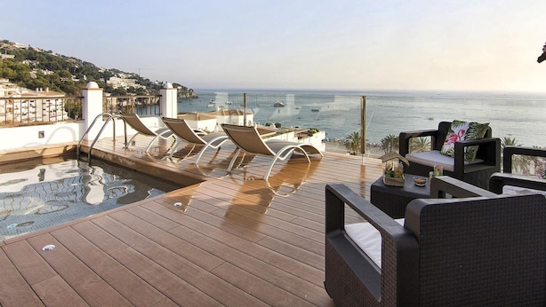 Une terrasse avec une piscine, des chaises longues et une table offrant une vue sur la mer et une côte lointaine.