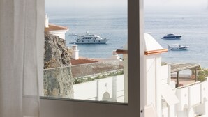 Une vue sur la côte, avec des bateaux sur l’eau, une falaise rocheuse et un bâtiment blanc doté d’un toit en tuiles.
