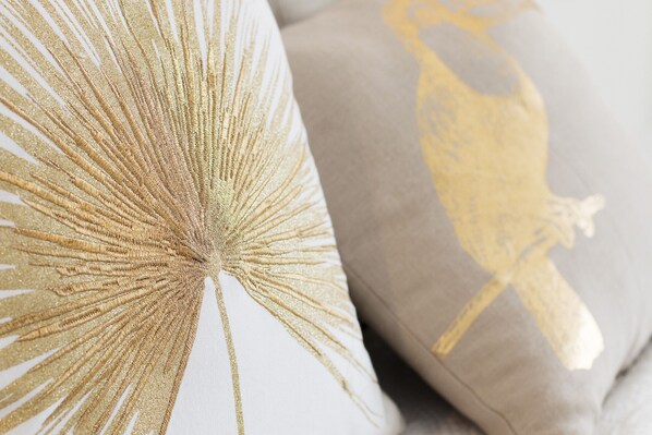 A close-up of a pillow with a golden feather pattern and another pillow with a golden bird design.