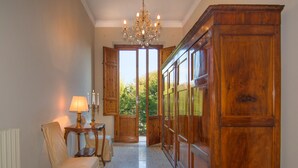 A hallway with a wooden cabinet, a table with a lamp, and a chair. - Villa Ricci Suites (Lucca)