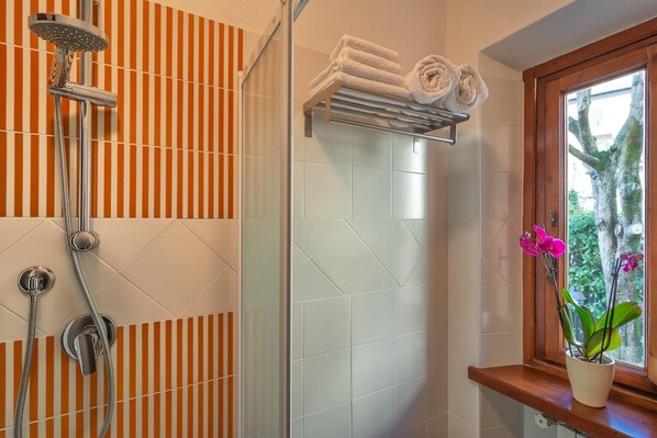 A bathroom with striped tiles, a shower, a towel rack, and a window with a plant.