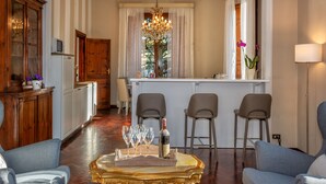 A spacious living room with a wooden cabinet, a chandelier, and a dining area with bar stools. - Villa Ricci Suites (Lucca)