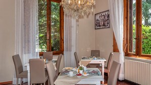 A dining area with a chandelier, dining tables, chairs, and a view of greenery outside. - Villa Ricci Suites (Lucca)