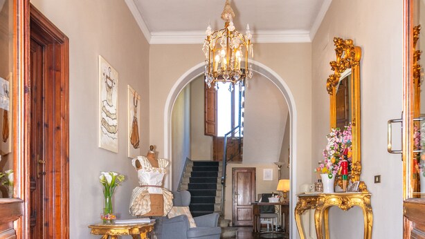A grand hallway with a chandelier, a blue armchair, and a gold-framed mirror. - Villa Ricci Suites (Lucca)