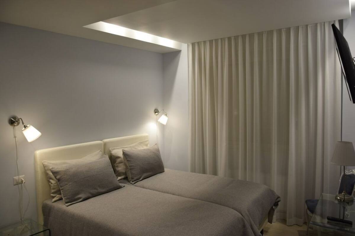A hotel room with a bed, two bedside lamps, a TV, and a window with curtains.