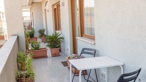 Un balcón con plantas en macetas, una mesa blanca y dos sillas.