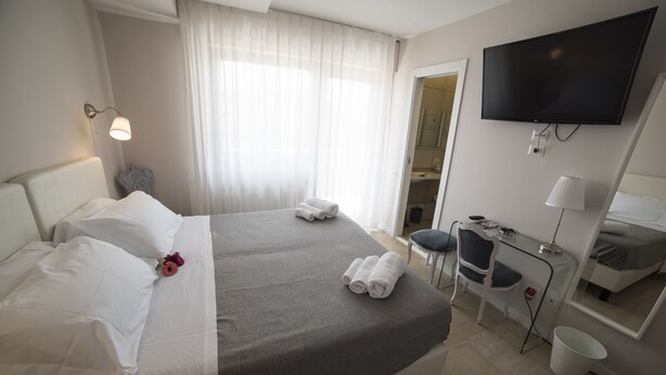 Habitación de hotel con cama, escritorio, silla, televisión y baño visible a través de una puerta abierta.