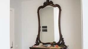 Una habitación con un espejo grande y decorativo sobre una consola de madera oscura, una puerta blanca y suelo de baldosas color beige.