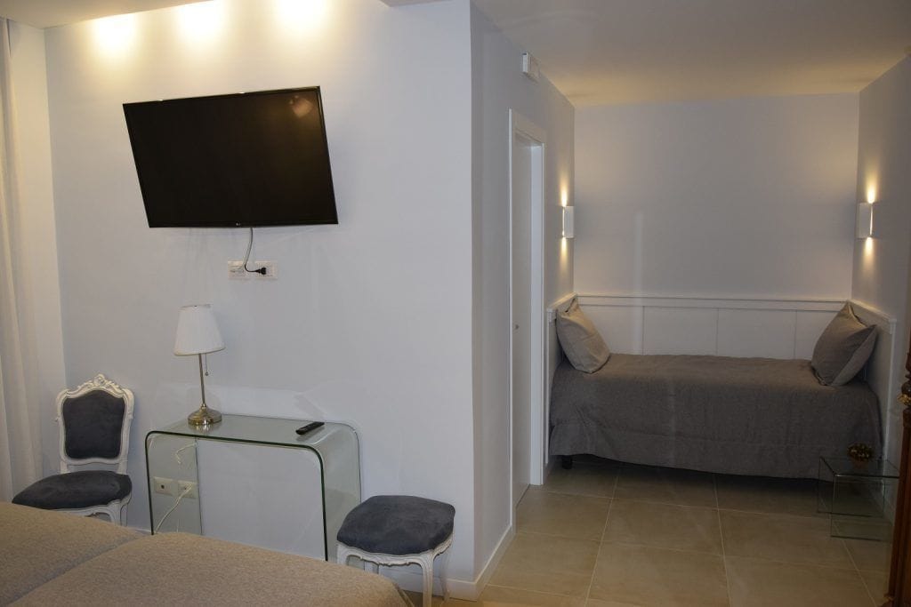 A hotel room with a bed, a desk with a lamp, a chair, a television mounted on the wall, and a small table.