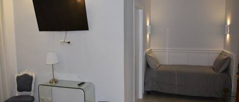 A hotel room with a bed, a desk with a lamp, a chair, a television mounted on the wall, and a small table.