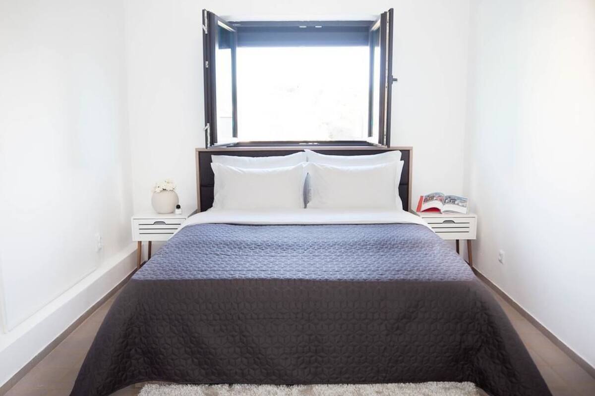 A bedroom with a bed, a window, a bedside table, and a nightstand.