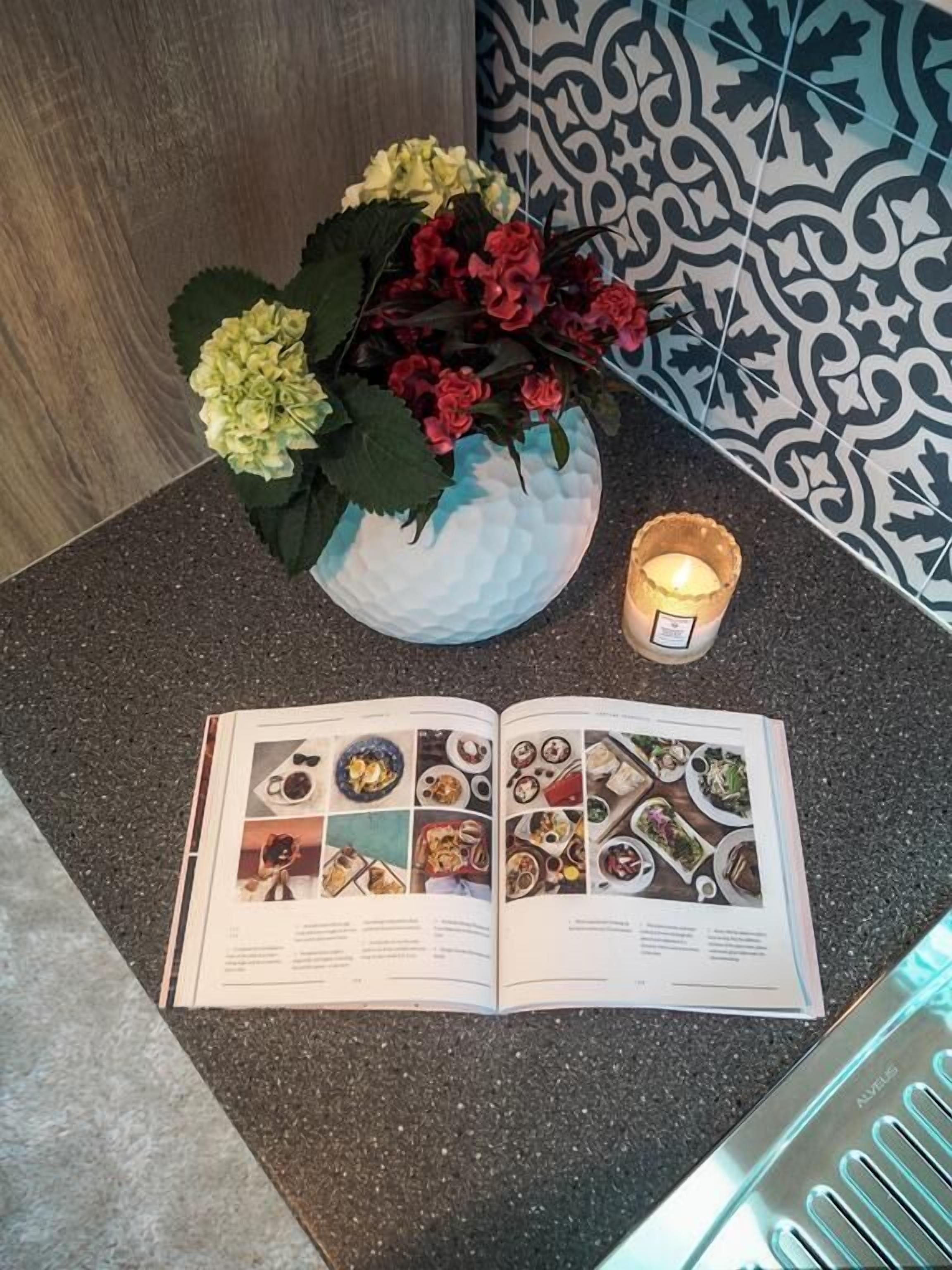 A magazine open on a countertop with a candle and a vase of flowers.