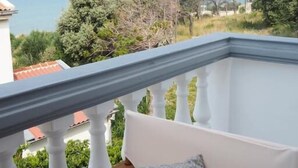 A balcony with a white railing, a white cushioned chair, and a patterned pillow. - Villa Lotus (Pag)