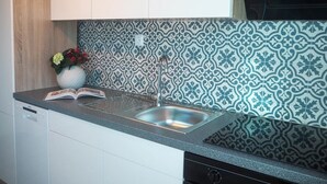 A kitchen with a patterned backsplash, a stainless steel sink, and a vase with flowers on the counter. - Villa Lotus (Pag)