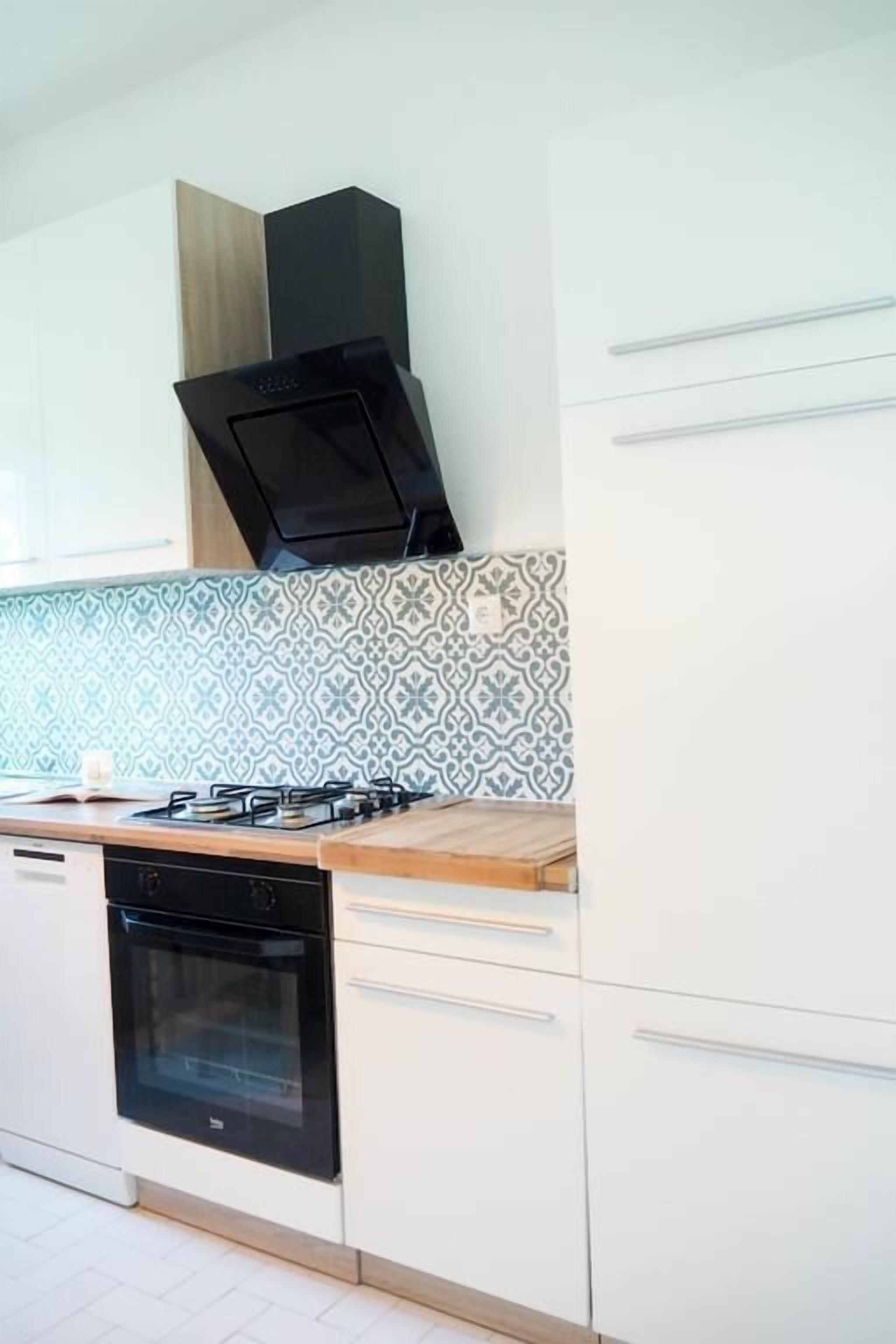A modern kitchen with white cabinets, a black stove, and patterned backsplash tiles.