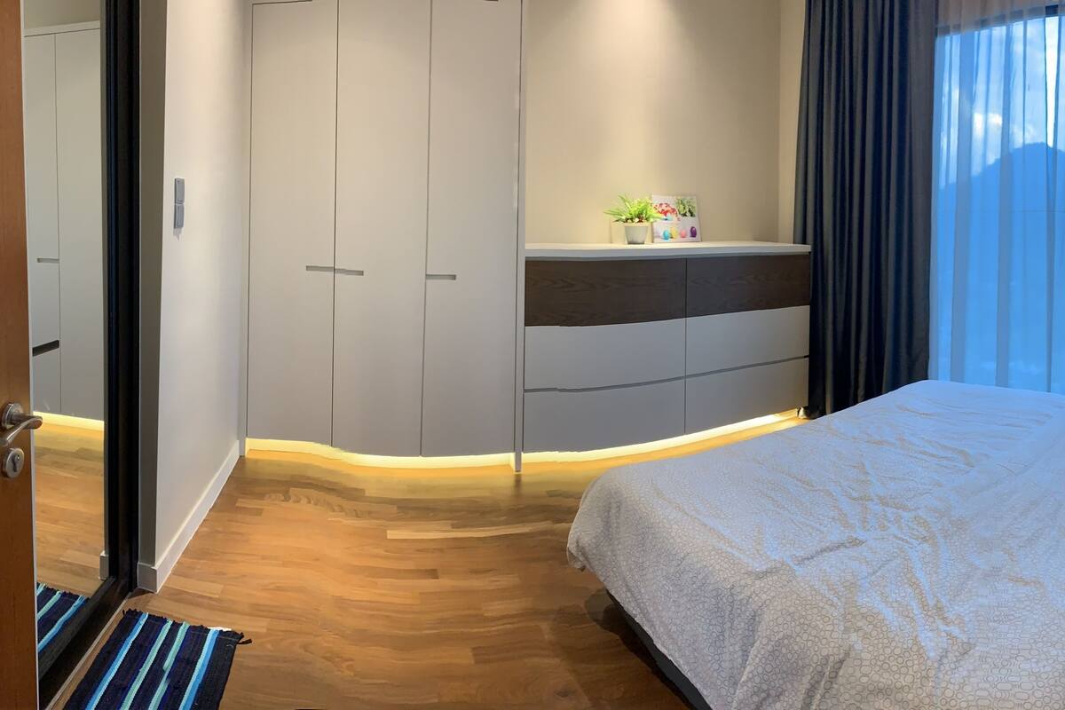 Quarto com cama, guarda-roupa, mesa de cabeceira com planta e janela com cortinas.