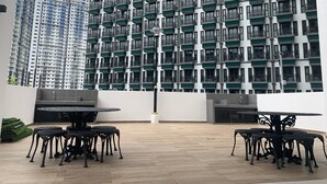 Een terras op het dak met een moderne zithoek, uitzicht op een hoog gebouw met balkons en een plat dak.