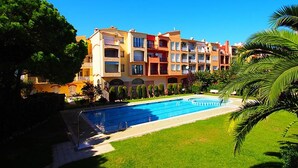 Ein mehrstöckiges Hotel mit Schwimmbad, umgeben von viel Grün und Palmen.