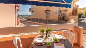 Ein Balkon mit Tisch für zwei Personen, einer blauen Markise und Blick auf die Straße und die Gebäude.