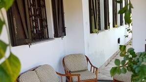 A covered outdoor seating area with two wicker chairs and a glass-top table, a tiled floor, and a white wall with windows. - Single villa from Titti and Carlo a stone's throw from the sea (Perd'e Sali)