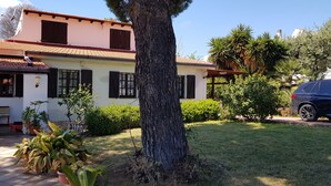 A two-story house with a tiled roof, a large tree in the front yard, and a parked car. - Single villa from Titti and Carlo a stone's throw from the sea (Perd'e Sali)