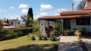 A house with a tiled roof, a covered porch, and a garden with various plants. - Single villa from Titti and Carlo a stone's throw from the sea (Perd'e Sali)