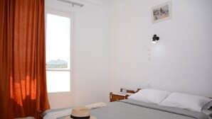 Une chambre à coucher comprenant un lit, une table de chevet, une fenêtre avec des rideaux et un luminaire fixé au mur.