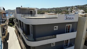Un bâtiment moderne doté de balcons, une enseigne indiquant « Miss Soul », et une vue sur une ville vallonnée en arrière-plan.