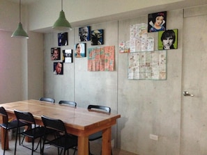 A dining area with a wooden table and chairs, a green pendant light, and various posters and maps on the wall.