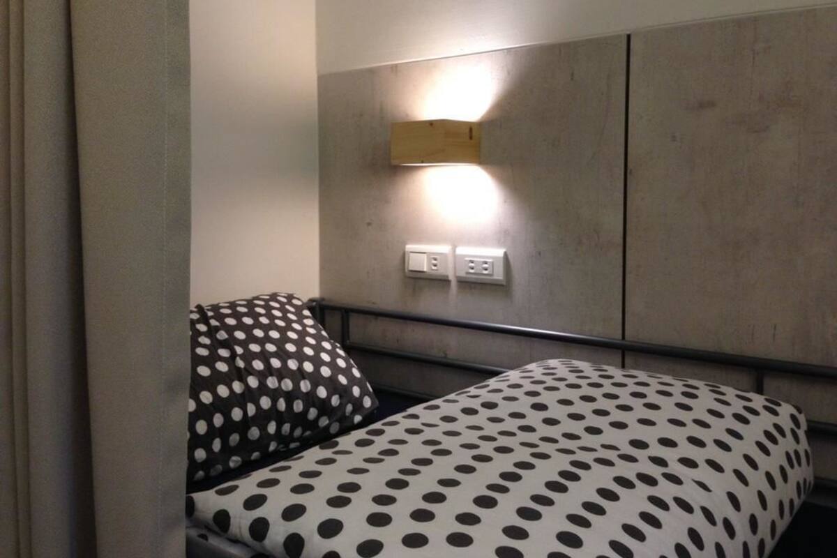 A hotel room with a bed featuring a polka dot bedspread, a headboard with a built-in light, and a wall-mounted power outlet.