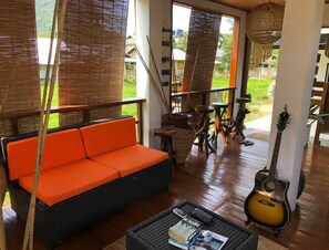 A room with a wicker sofa, a guitar, and a wicker coffee table with books.