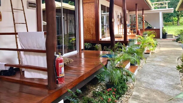 A covered outdoor area with wooden flooring, a fire extinguisher, and potted plants. - Bella Athena Garden (El Nido)