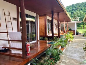 A covered outdoor area with wooden flooring, a fire extinguisher, and potted plants.