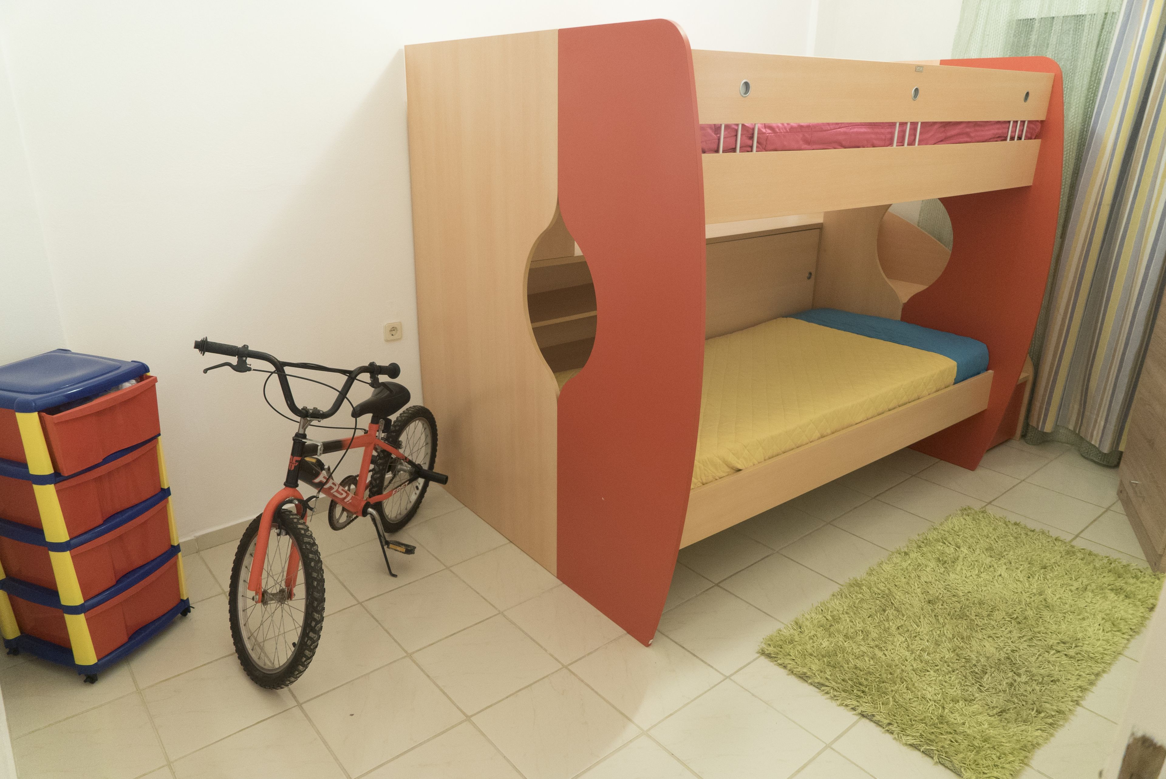 A bunk bed with a bicycle and storage unit in a room with a green rug.