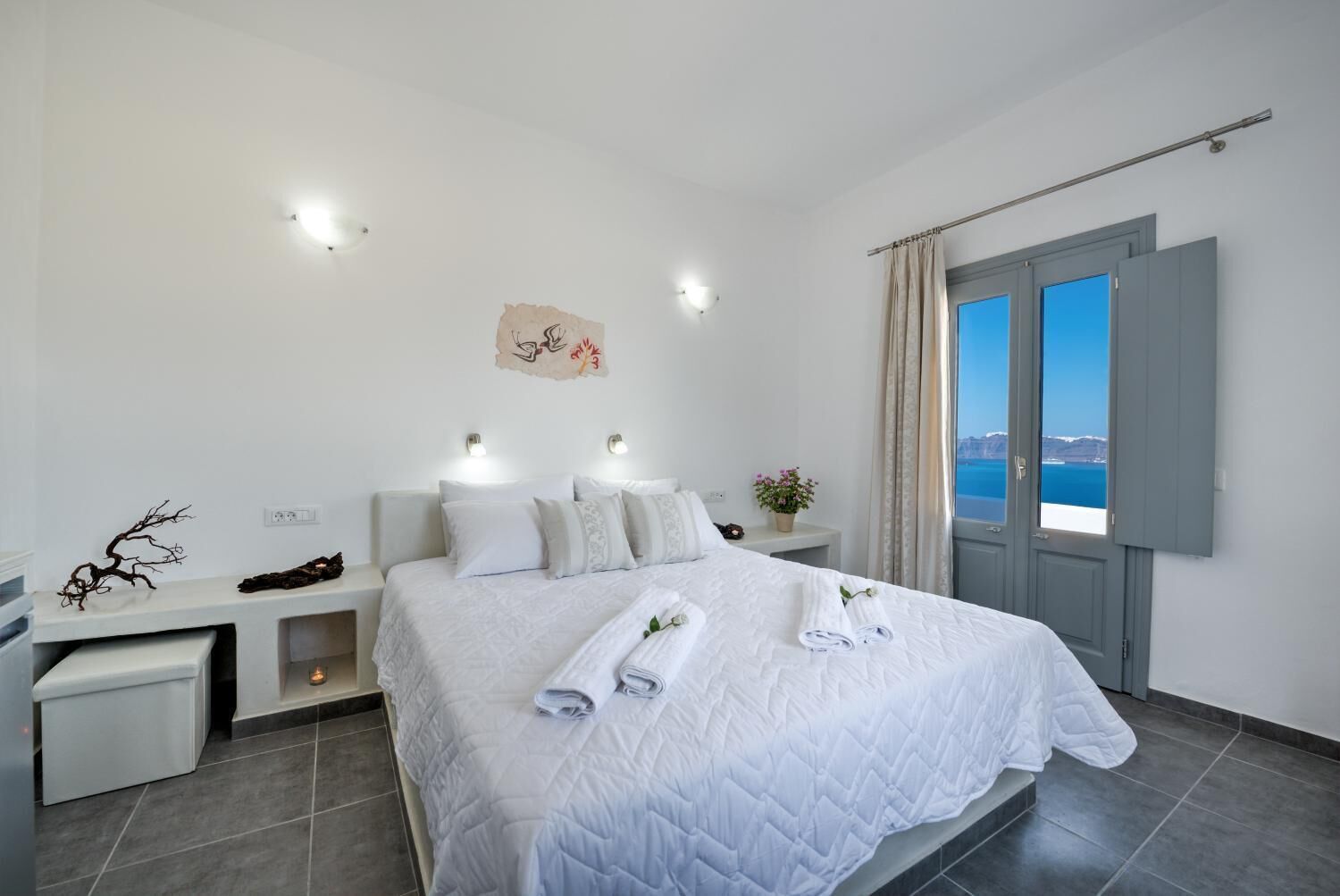Una habitación de hotel moderna con una cama grande, mesitas de noche, una ventana con cortinas y vistas al mar.