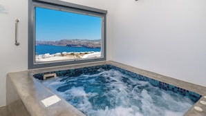 A hot tub with a view of a coastal landscape. - Pancratium villas & suites (Santorini)