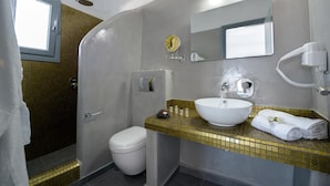 A bathroom with a white sink, a mirror, a towel, and a shower. - Pancratium villas & suites (Santorini)