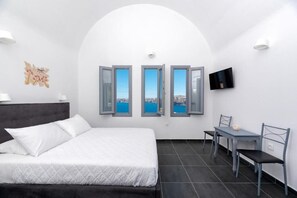 Un dormitorio con cama, escritorio y silla. Tres ventanas ofrecen vistas azules.