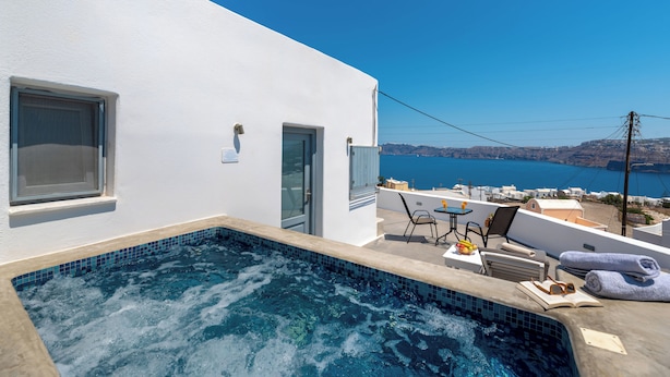 A rooftop pool with a clear view of the sea, a small table with chairs, and a door leading to the interior. - Pancratium villas & suites (Santorini)
