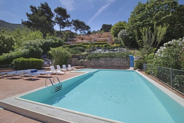 A rectangular swimming pool with a stone wall and a pergola in the background. - Residence Vistamare La Fonte (nisporto)