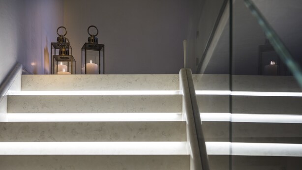 Un escalier avec une rampe en verre, deux bougies allumées et un mur en marbre.