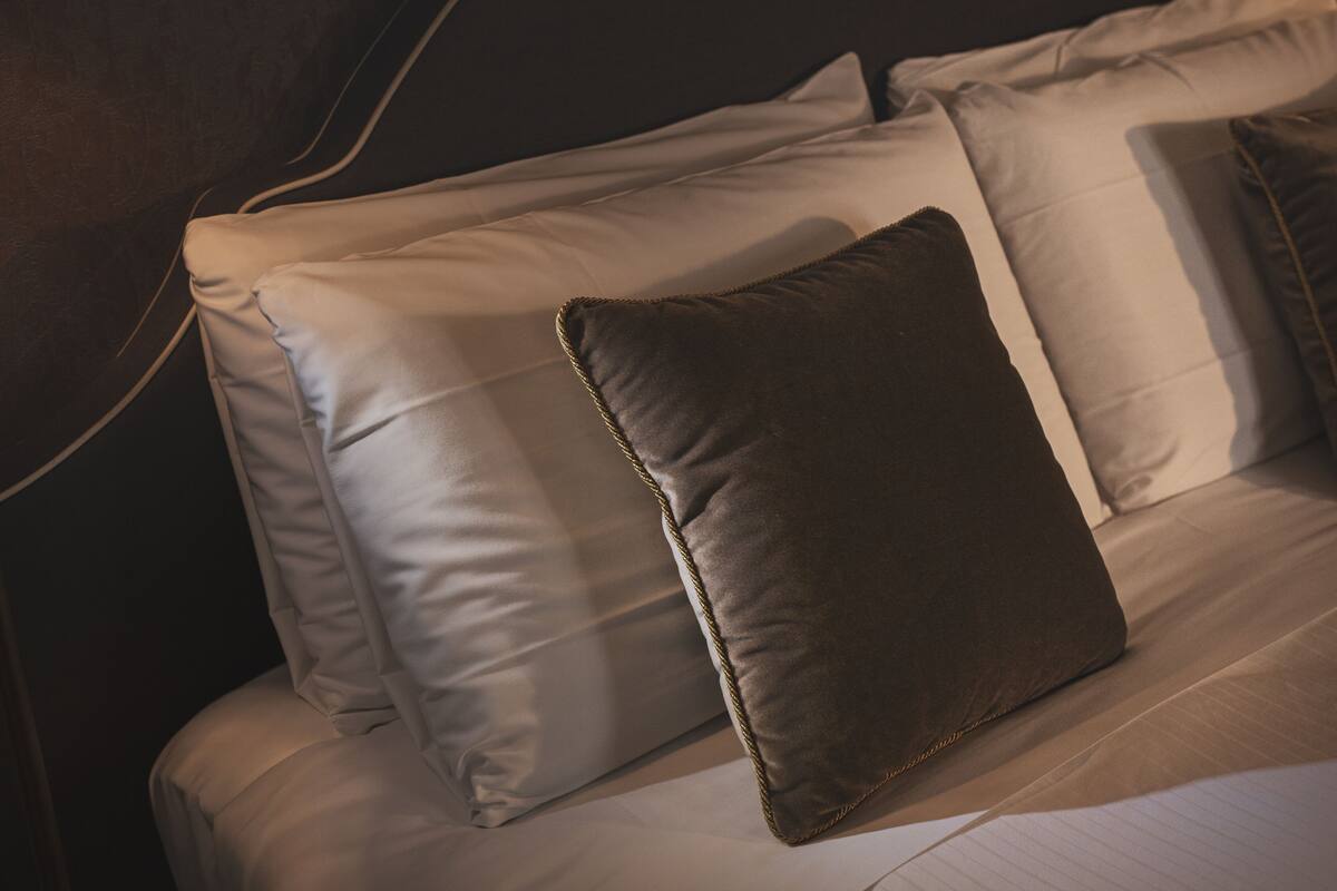 Una cama con ropa de cama blanca y una almohada marrón.