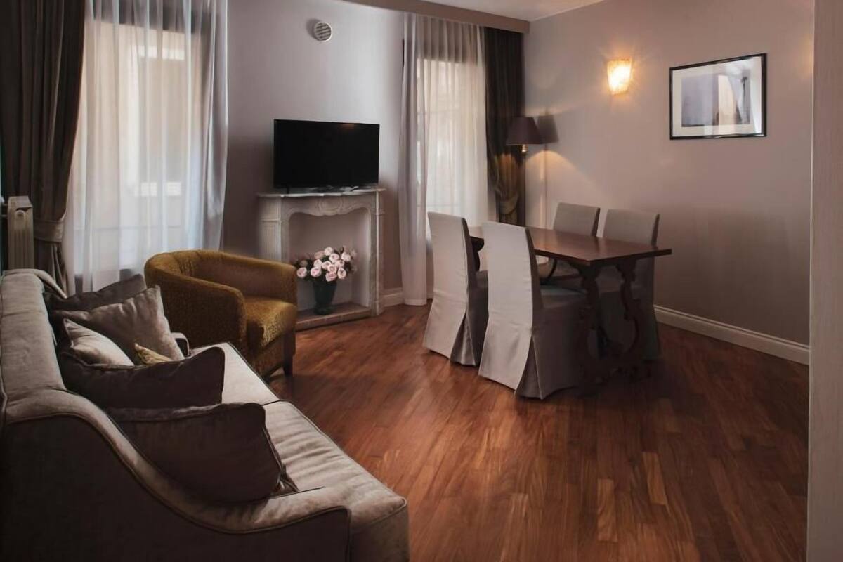 Una sala de estar con un sofá, una mesita, un televisor y un comedor con sillas.
