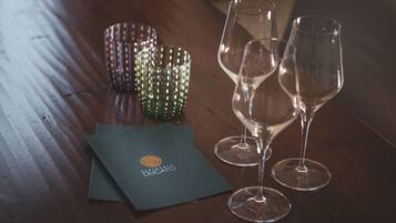 A wooden table with two empty wine glasses and a green patterned candle holder. A dark-colored envelope with a logo is also visible.