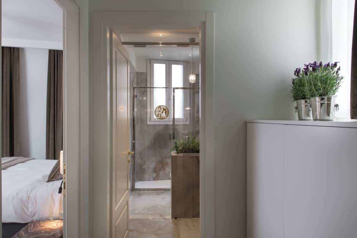 Una habitación de hotel moderna con cama, baño con ducha de vidrio y una planta en la encimera.