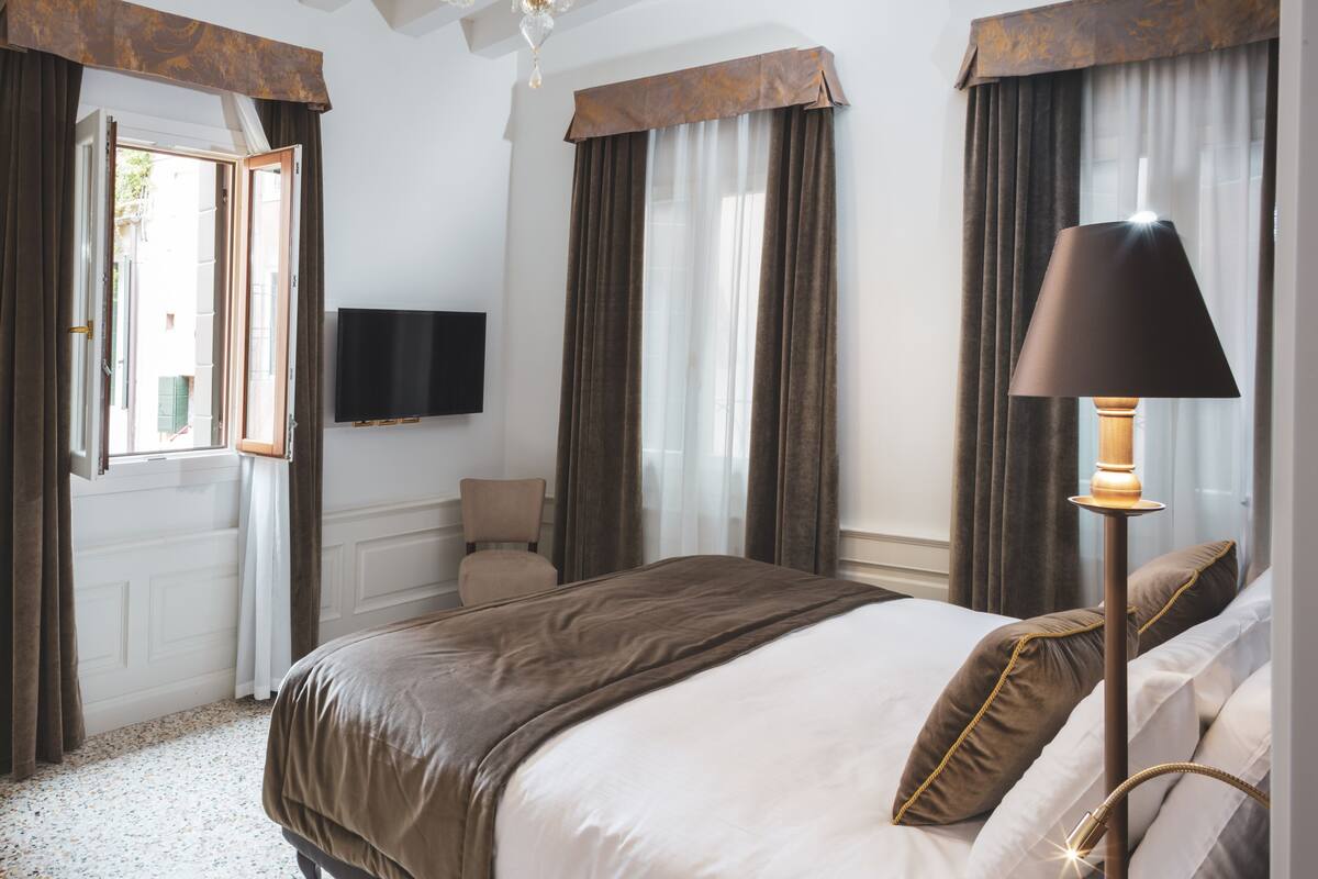 Una habitación de hotel con una cama grande, un televisor de pantalla plana, una araña y una lámpara de pie.