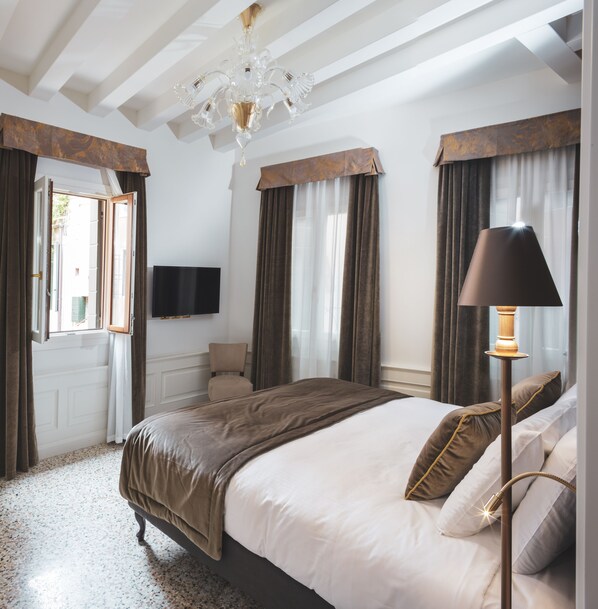 A hotel room with a large bed, a flat-screen TV, a chandelier, and a floor lamp.