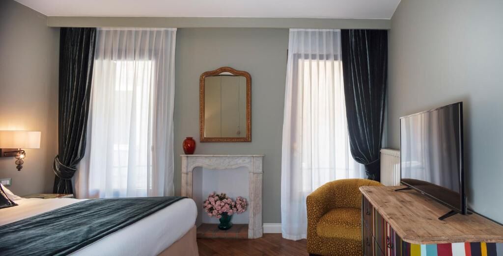 Una camera d'albergo con un letto, un tavolino con la televisione, un camino e una poltrona.