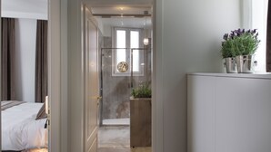 Une chambre d’hôtel moderne avec un lit, une salle de bain dotée d’une douche en verre et une plante en pot posée sur le comptoir.